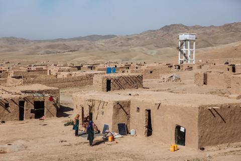 A village in a desert landscape with a white tower in the background